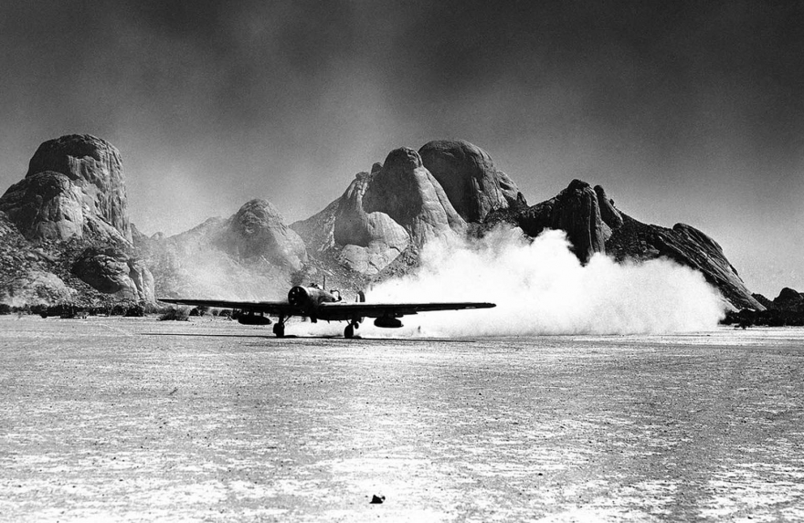 На фоне скального образования британский бомбардировщик взлетает 15 мая 1941 года из Восточной Африки, оставляя за собой след дыма и песка.